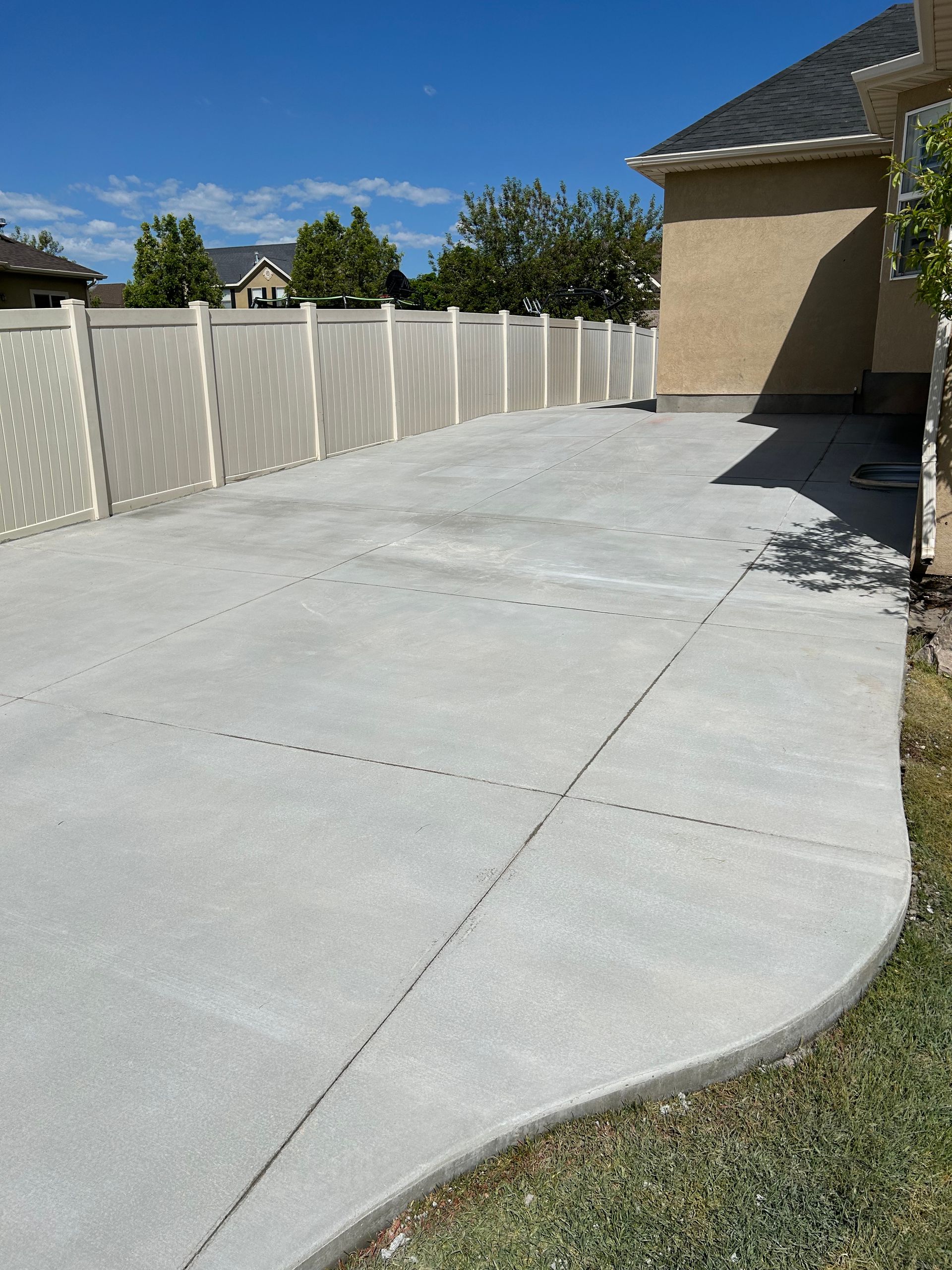 Concrete driveway beside a beige house and white fence on a sunny day