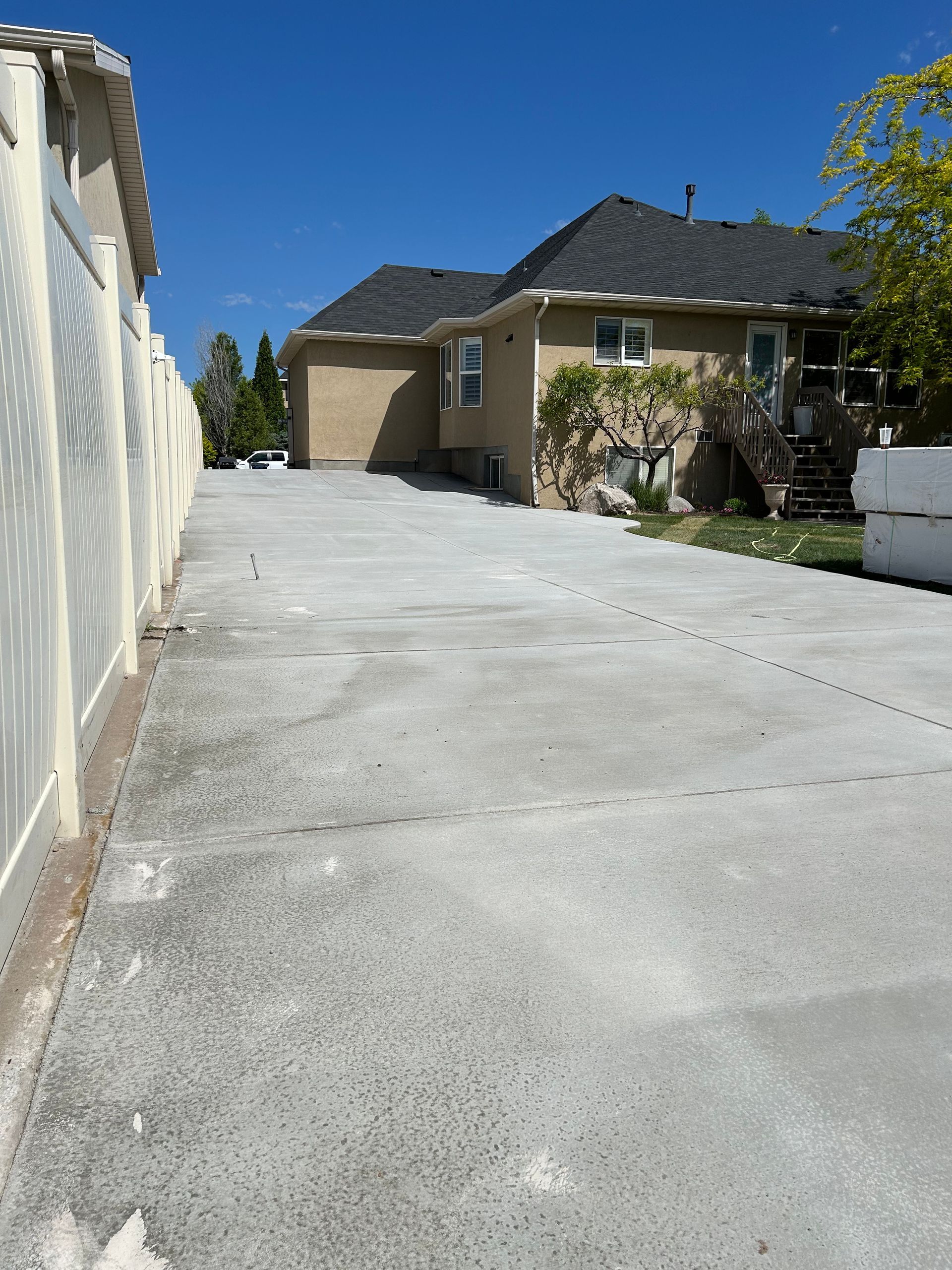 Long concrete driveway leading to a beige house and garage under a clear blue sky