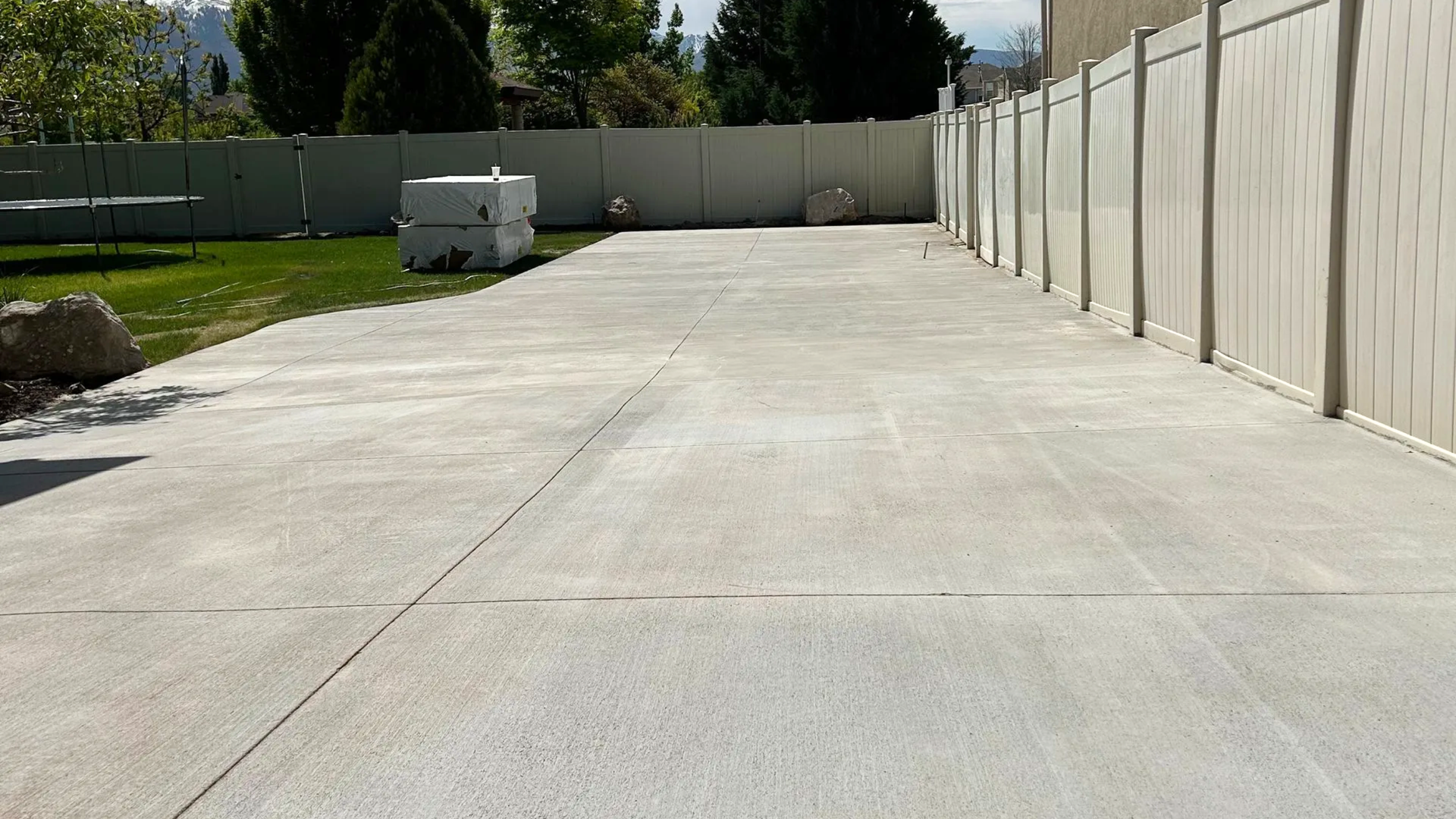 Freshly poured and finished concrete patio slab in a backyard in Syracuse Utah with vinyl fence and