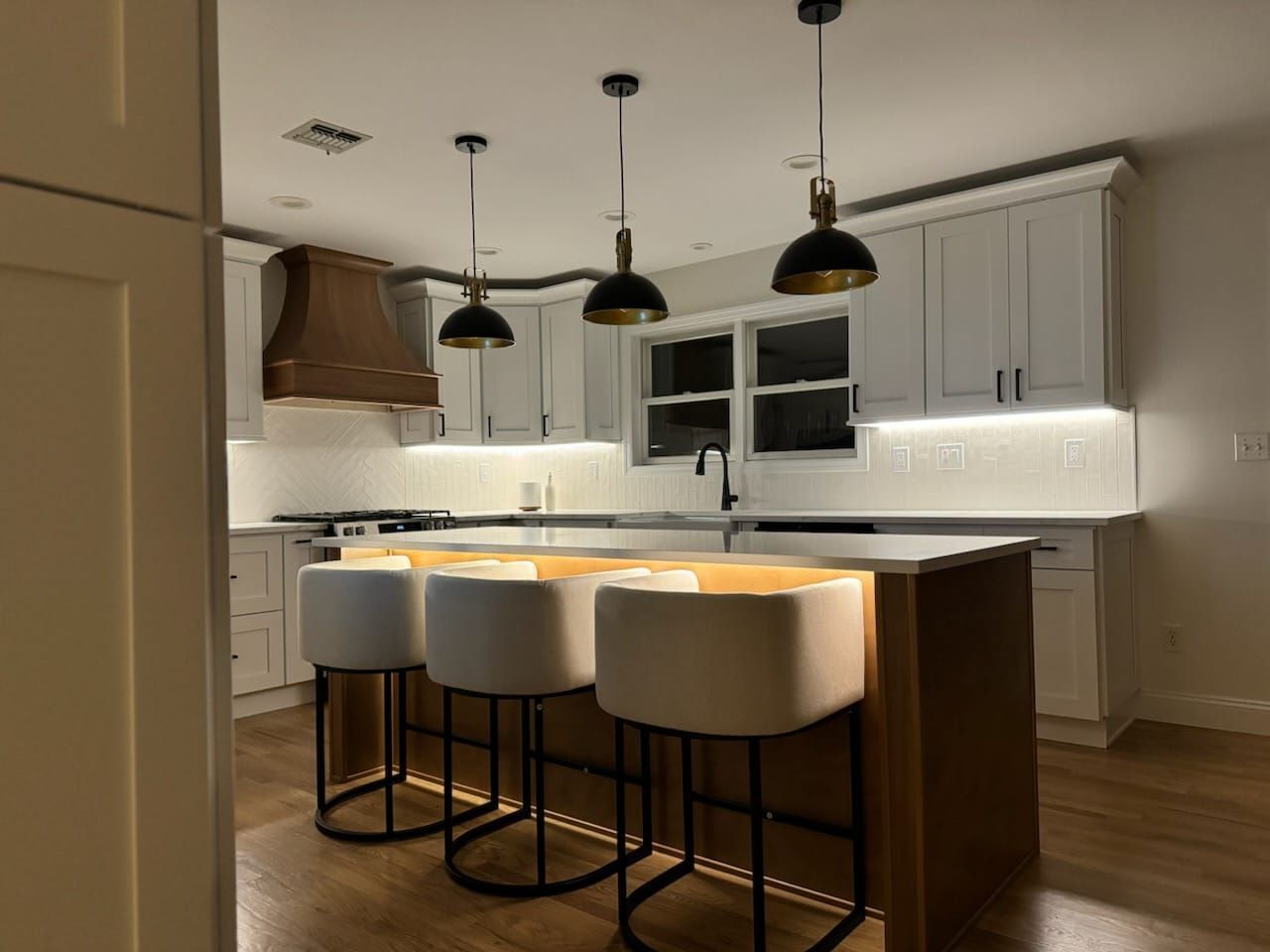Modern kitchen with island, four cream stools, pendant lights, and gray cabinets