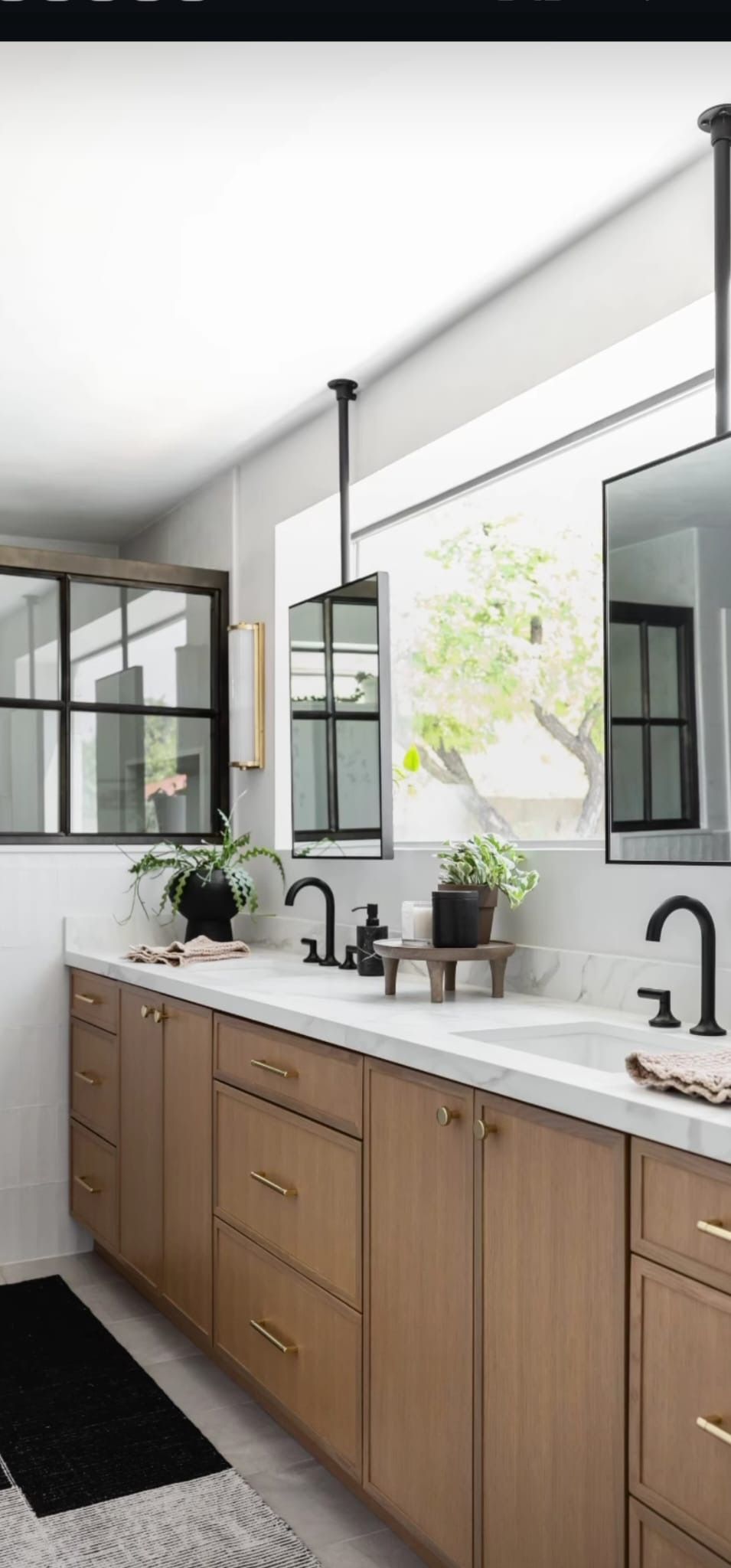 Bright bathroom with wood vanity, black fixtures, large mirror, and natural light from a window