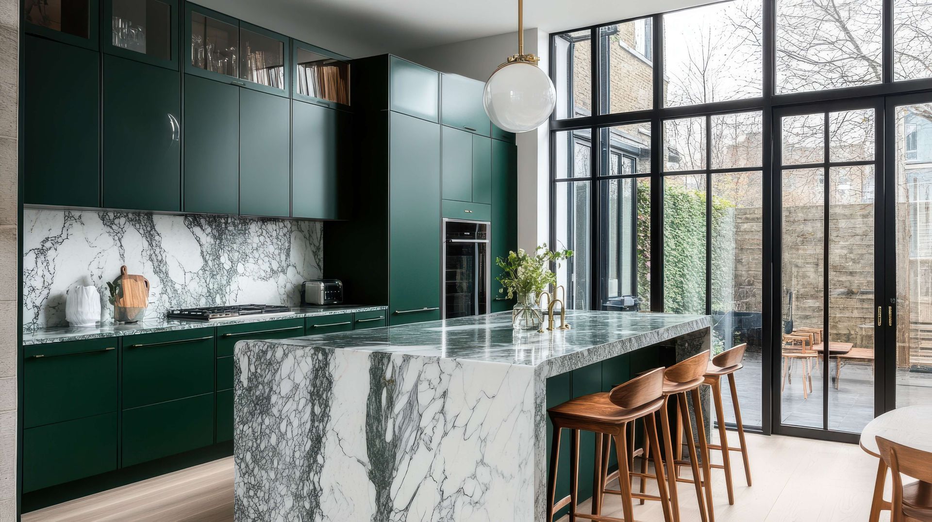 Modern kitchen with dark green cabinets, marble island, and bar stools by large glass doors