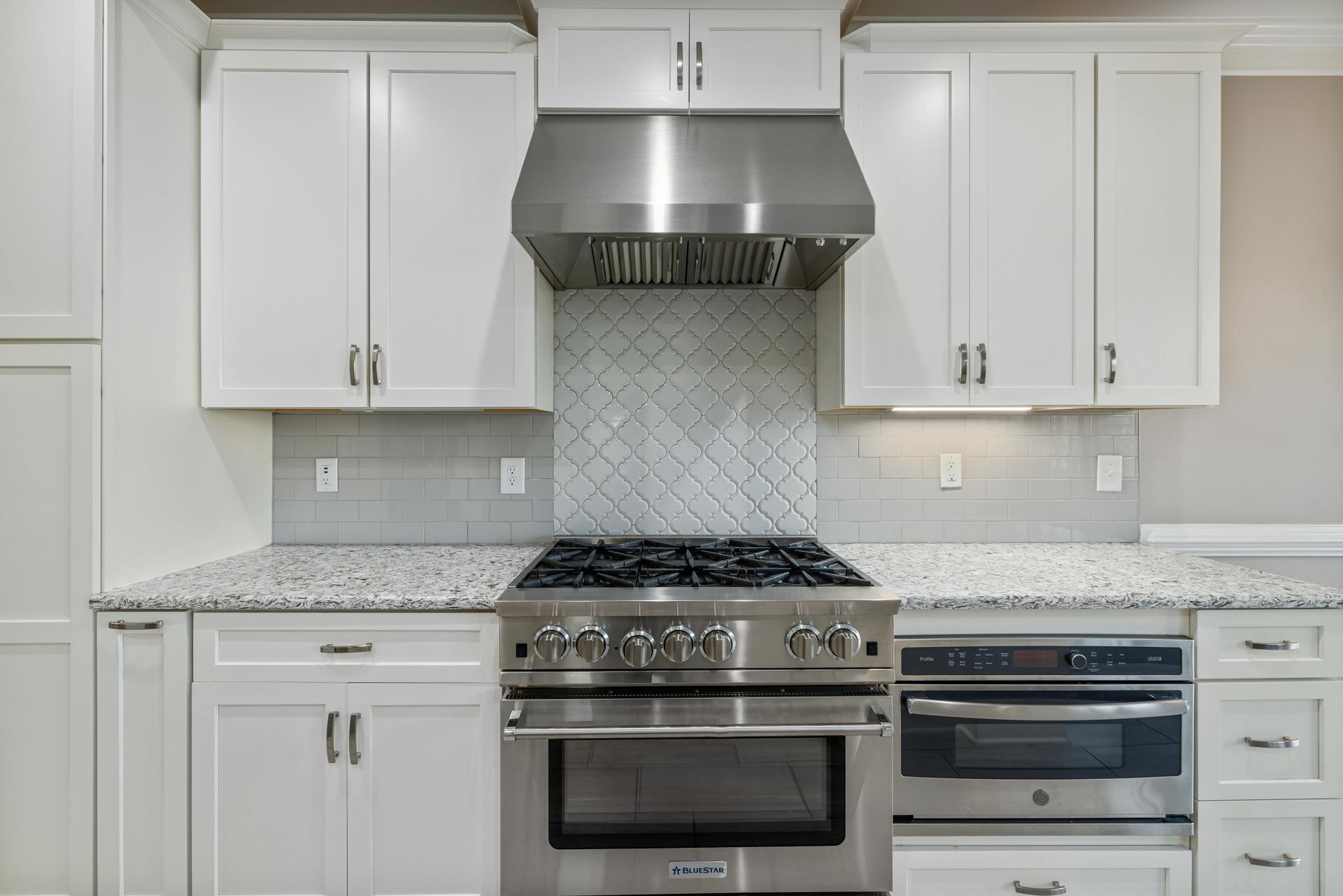 Modern white kitchen with granite countertops, stainless steel stove and hood, and white cabinets.