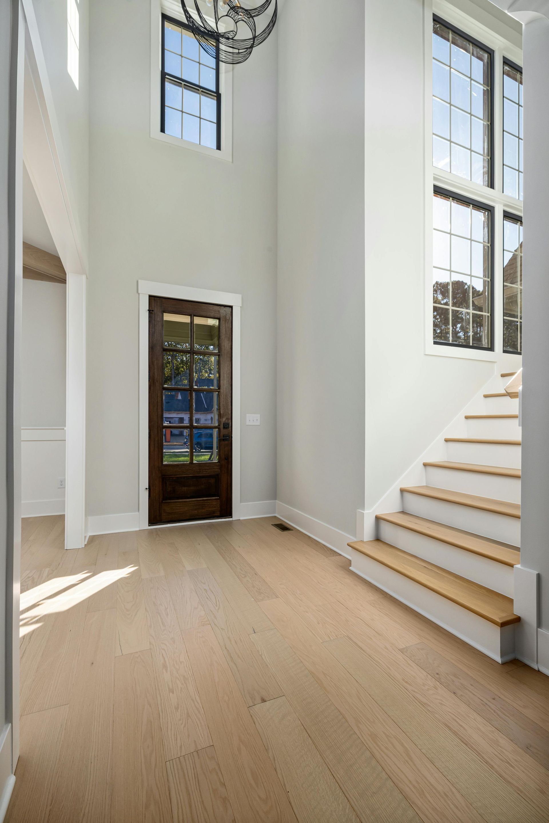 Bright foyer with white walls, light wood floors, tall windows, and a staircase on the right.