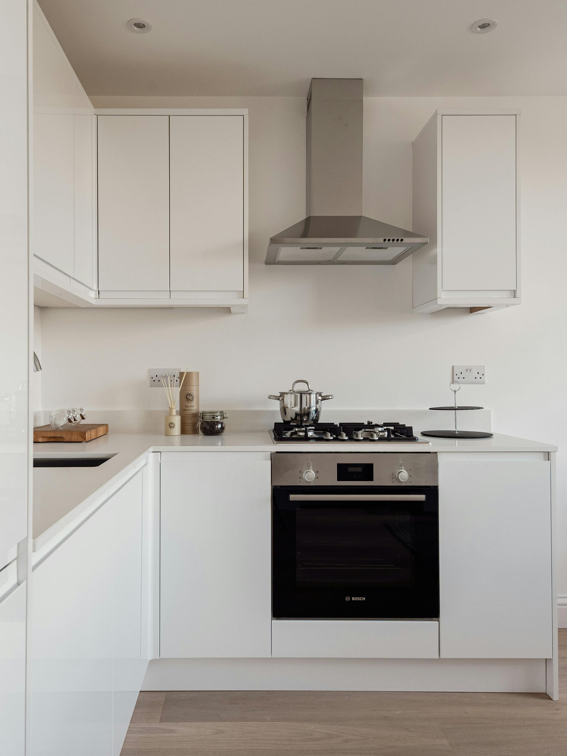 Modern white kitchen with stainless steel oven, stovetop, range hood, and cabinets