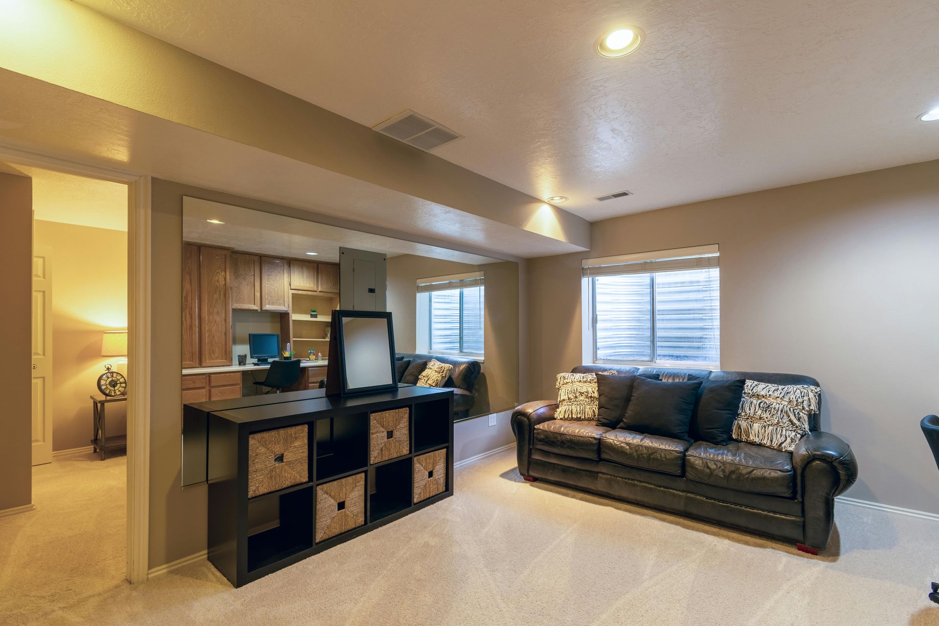 Modern living room with a black sofa, cubby storage console, and bright windows with blinds.