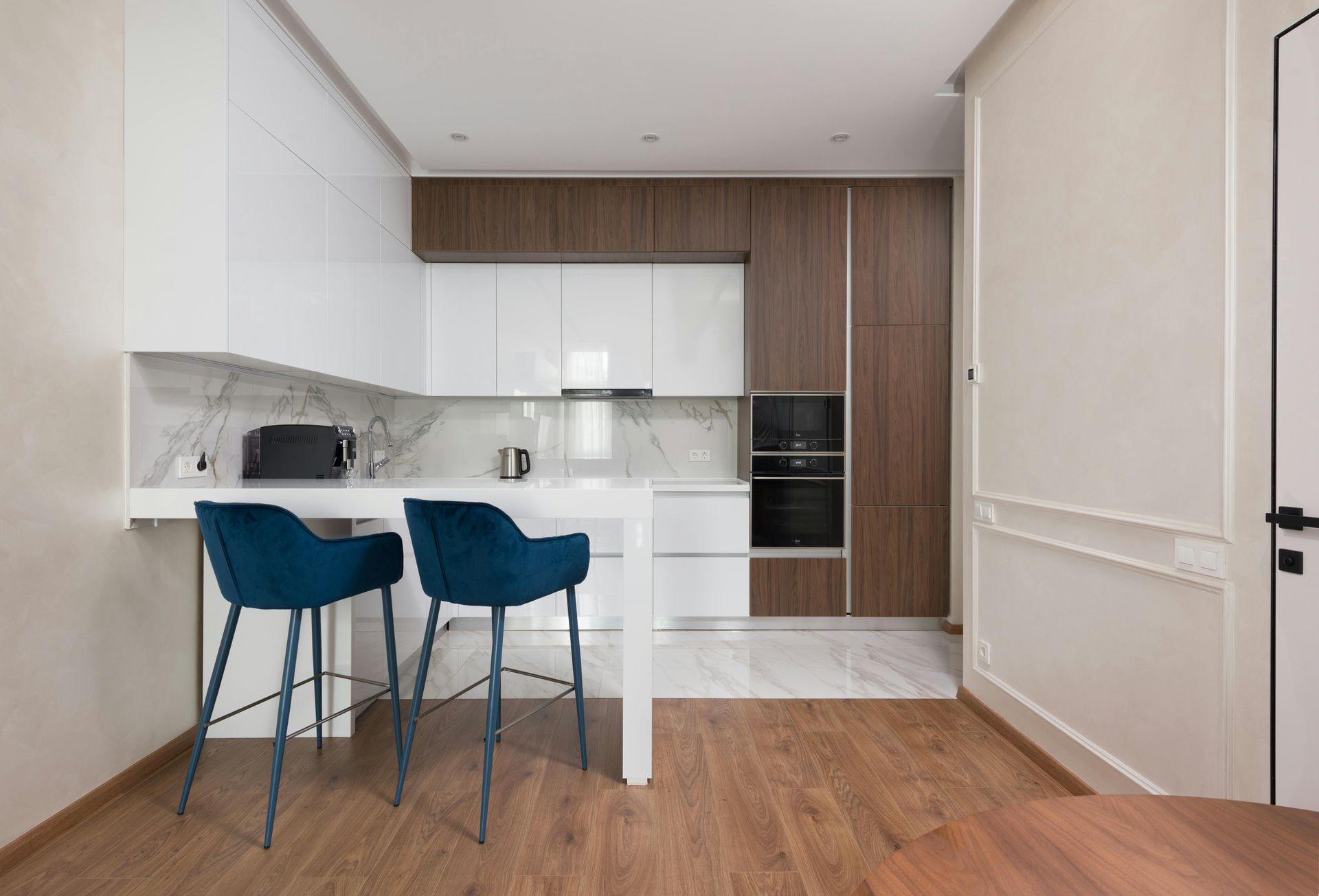 Modern kitchen with white cabinets, wood accents, and two blue bar stools at a breakfast counter