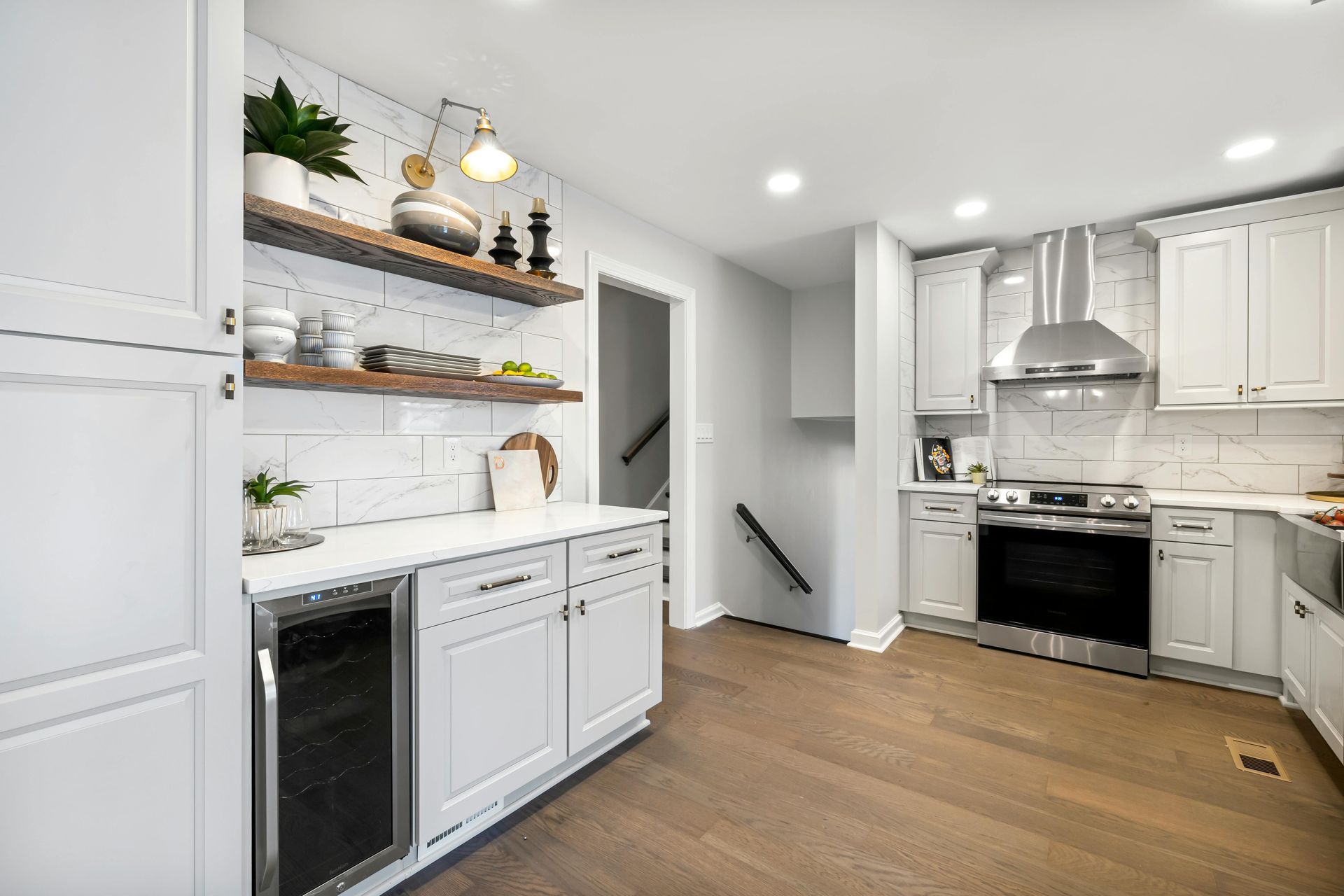 Bright modern kitchen with white cabinets, wood floors, open shelves, and stainless steel appliances.
