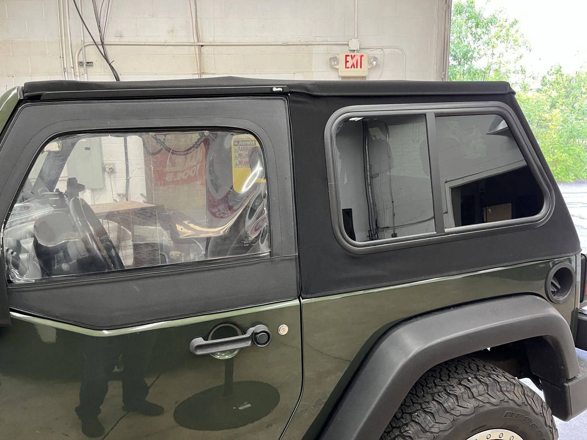 A green jeep with a black top is parked in front of a building