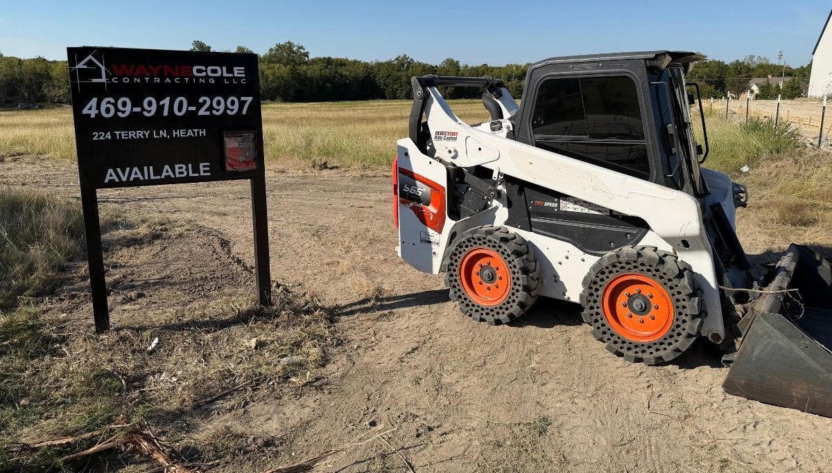 White Bobcat skid steer beside a real estate sign on a dirt lot.