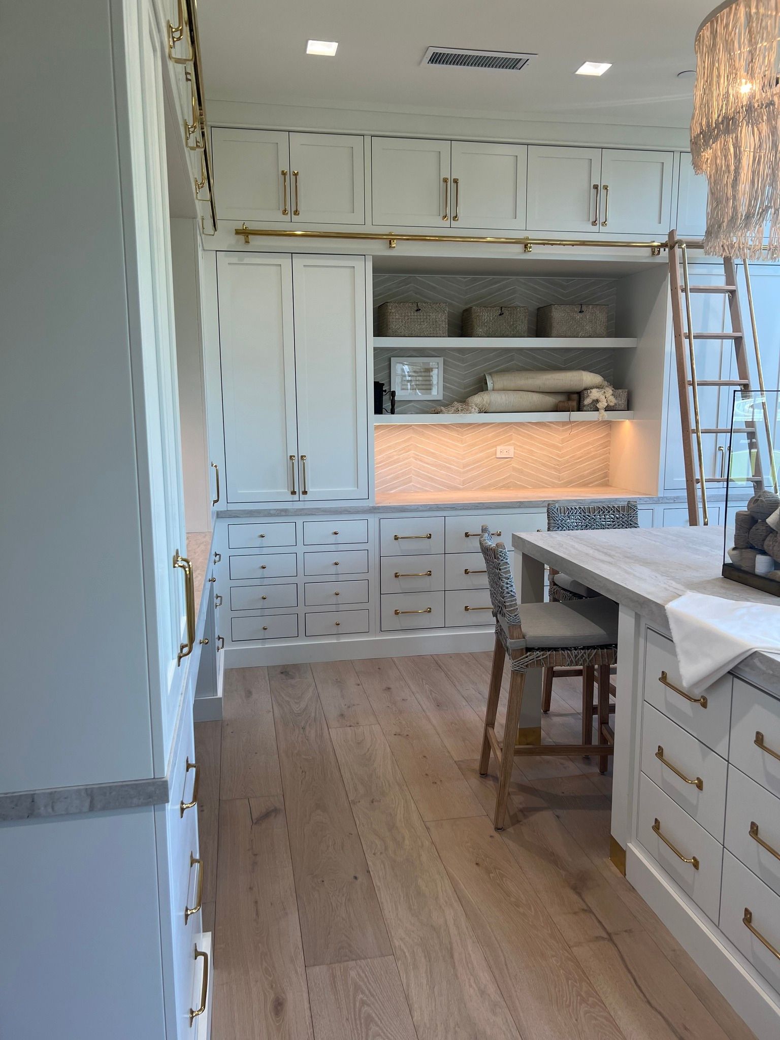 Bright white kitchen with built-in cabinets, wood floor, island, and a ladder near an open upper cabinet.