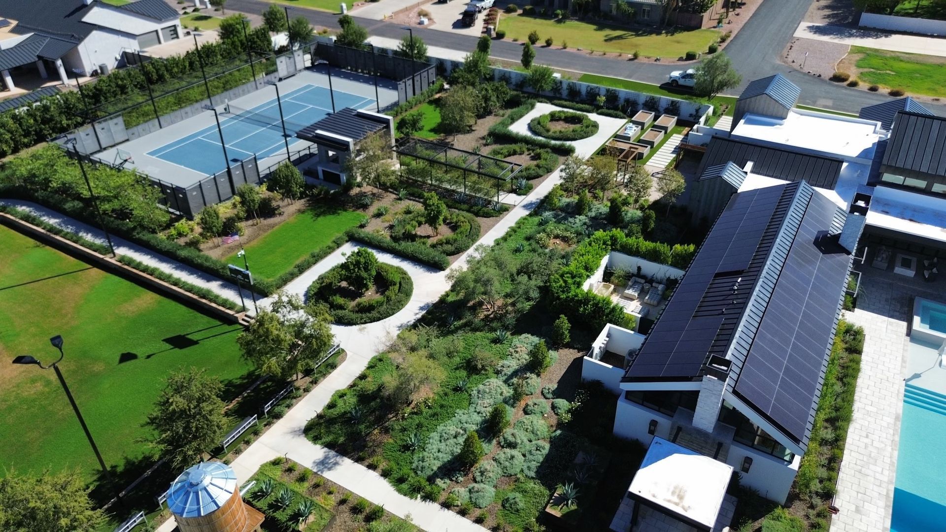 Aerial view of a landscaped garden with paths, trees, tennis courts, and surrounding buildings