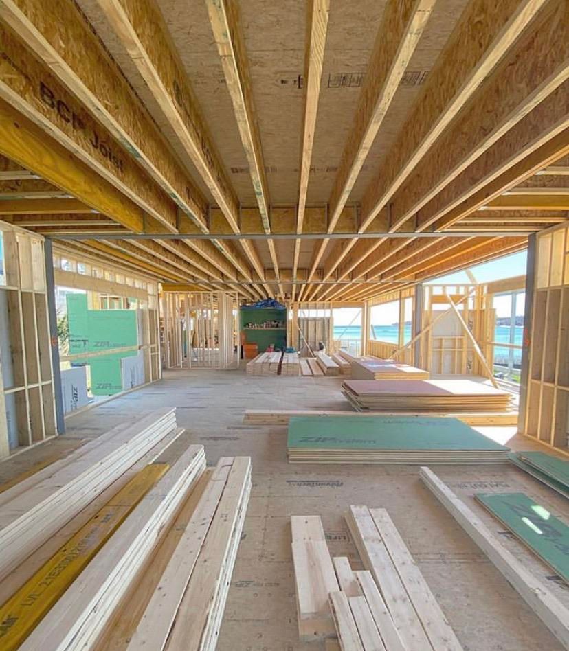 Unfinished house interior with exposed wooden framing, beams, and stacked lumber under construction.