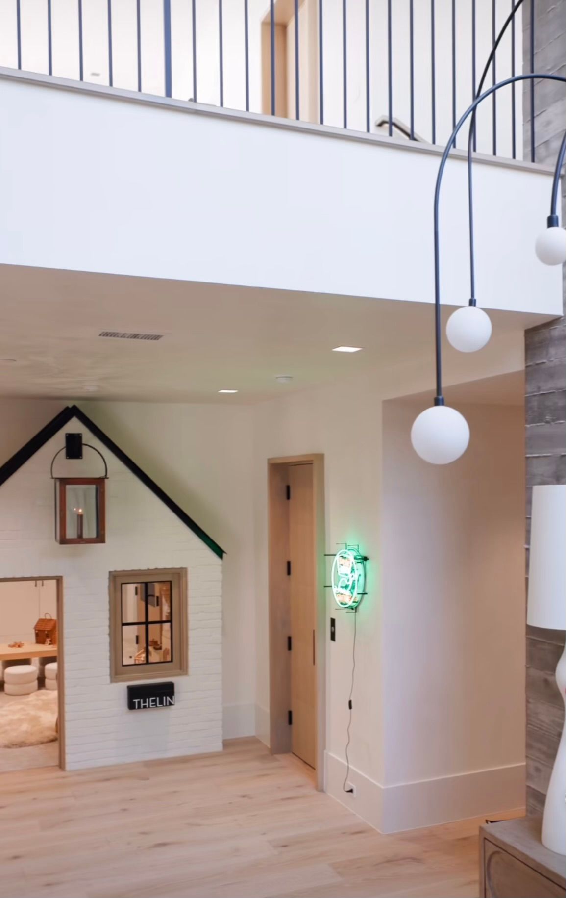 Modern home interior with loft railing, staircase, and a small playhouse-style doorway on a wooden floor