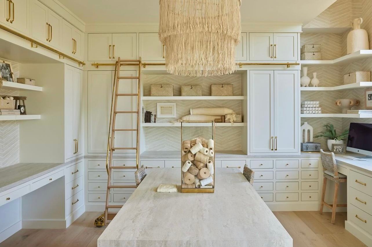 Bright built-in home office with white cabinetry, ladder, desk, and a woven chandelier