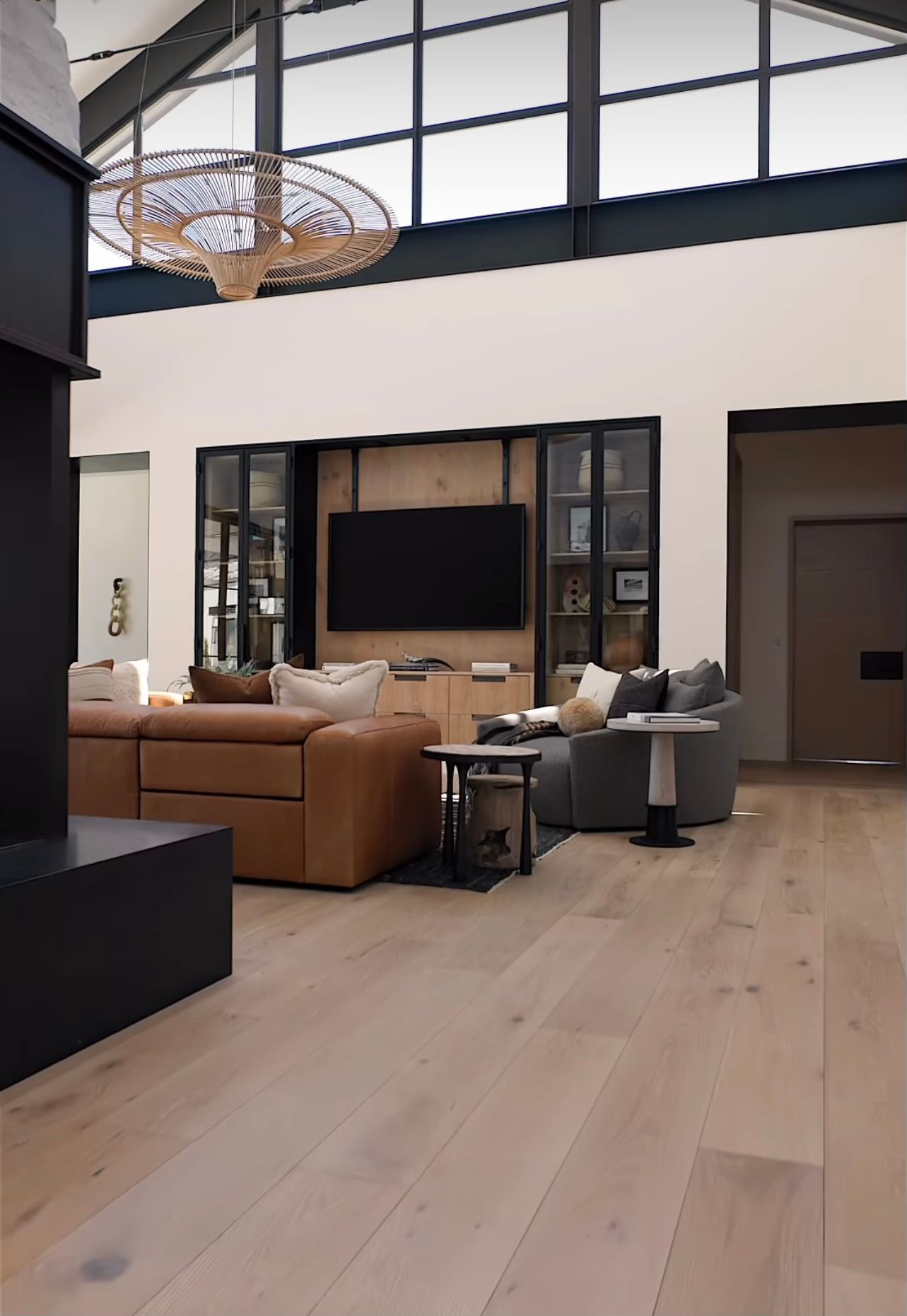 Modern living room with tan sectional, wall-mounted TV, high windows, and light wood floors