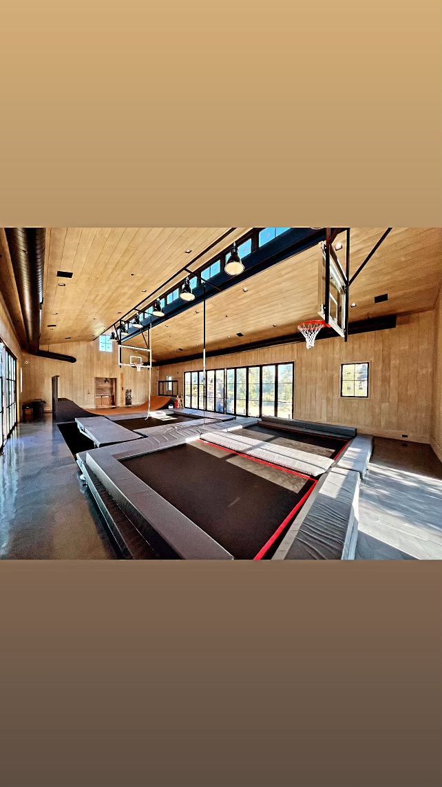 Indoor gymnasium with wooden walls, a basketball hoop, and a central court under skylights