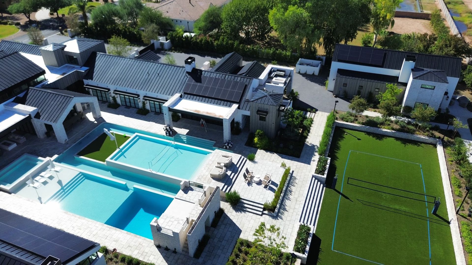 Aerial view of a modern home with a turquoise pool and large green sports court.