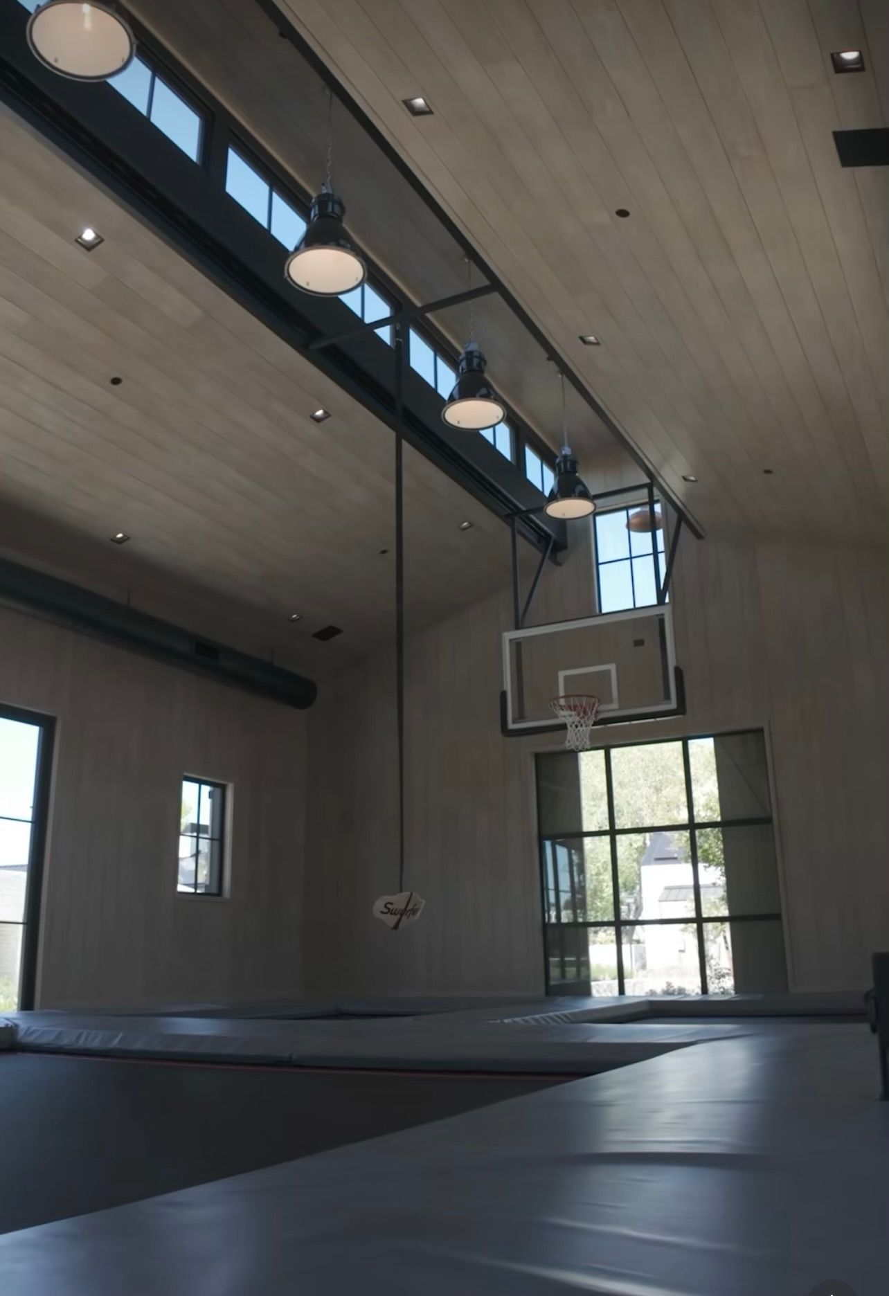 Modern indoor basketball court with high windows, hanging lights, and a hoop at one end