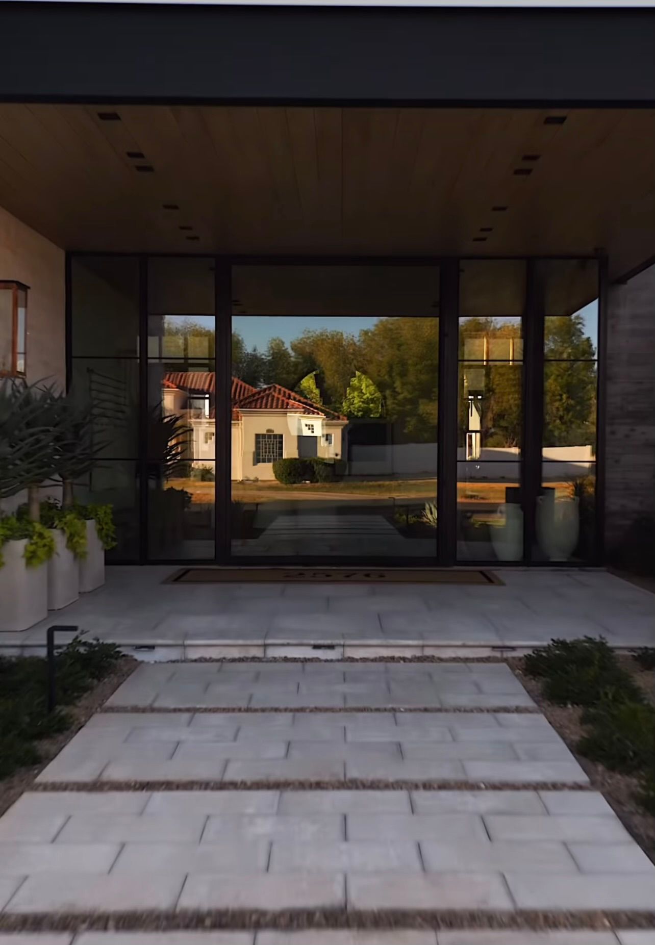 Modern house entrance with stone walkway, glass doors, and a landscaped courtyard reflected in the facade