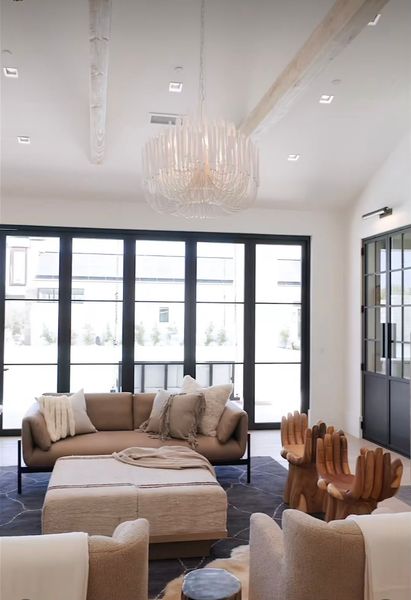 Modern living room with beige sofas, chandelier, and large black-framed windows