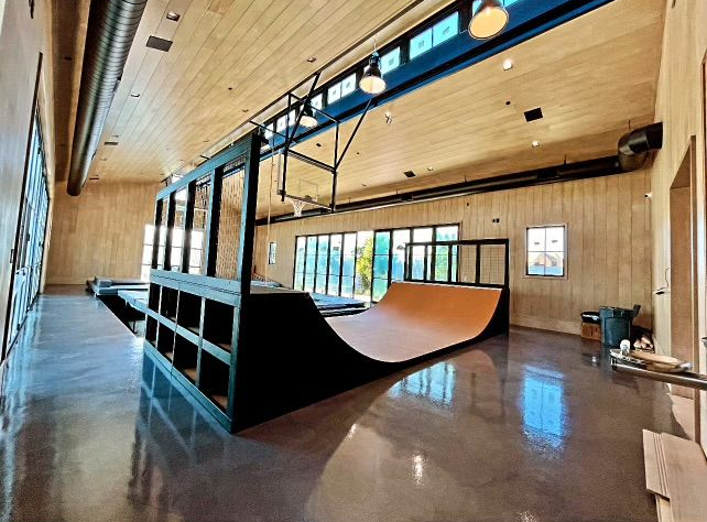 Indoor skate park with a black ramp in a wood-paneled hall and large windows.