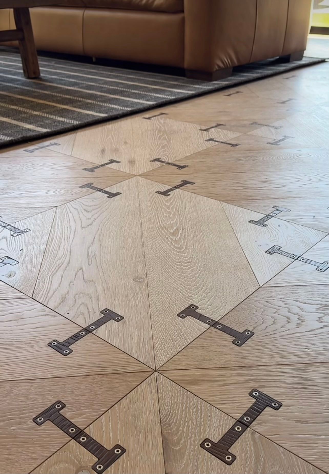 Close-up of light wood-pattern tile floor with dark metal inset connectors beside a sofa and rug.