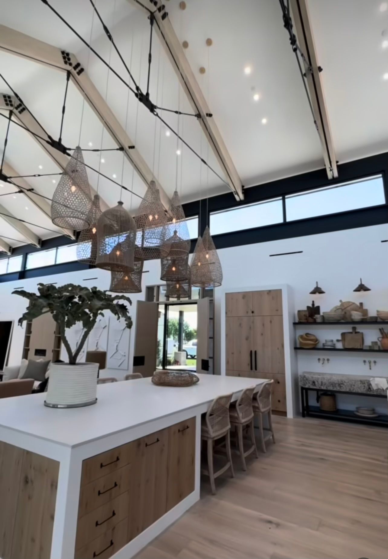 Bright, modern kitchen with white island, wooden stools, hanging lights, and open shelving.