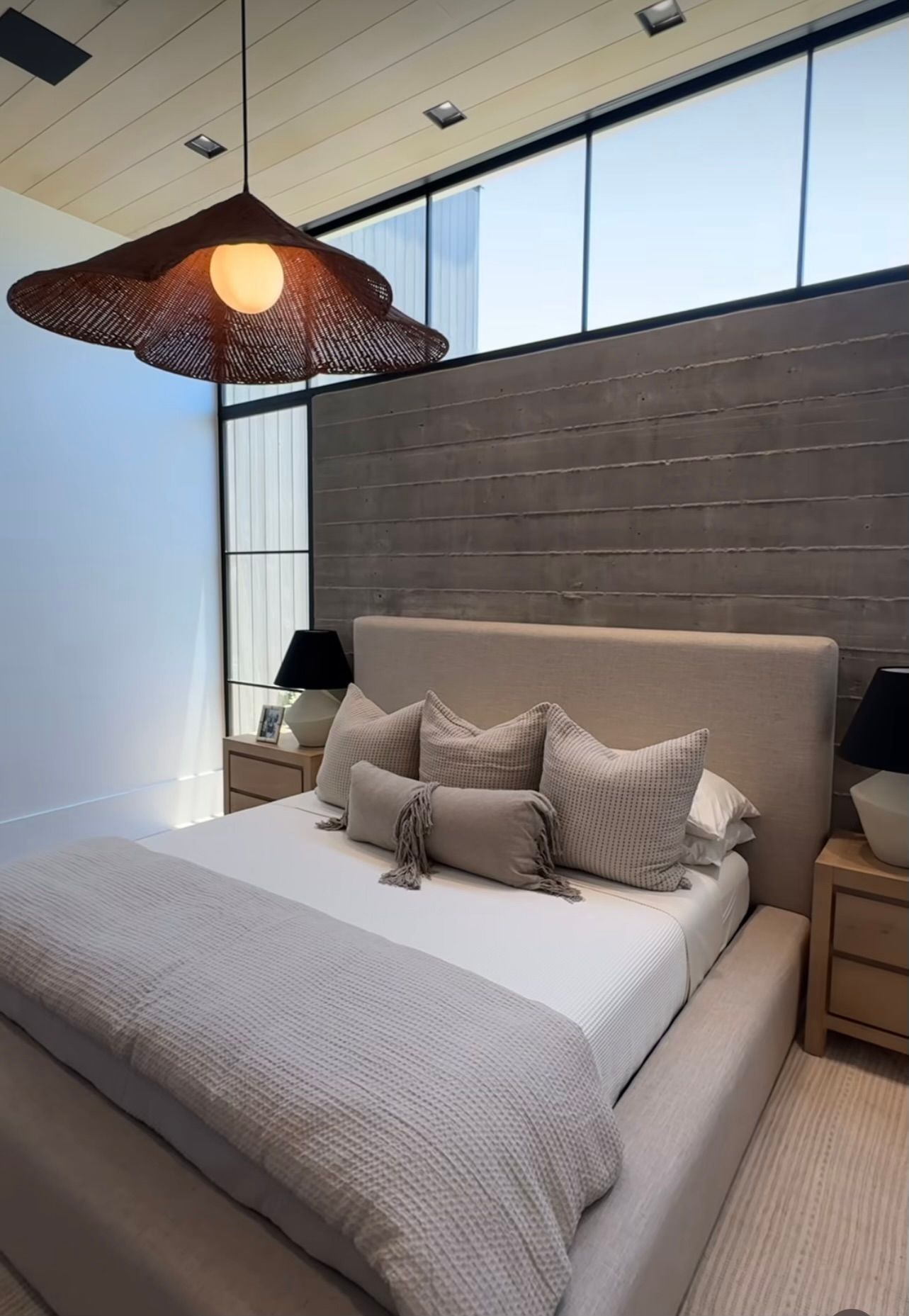 Modern bedroom with a bed, gray bedding, woven pendant light, and large windows.