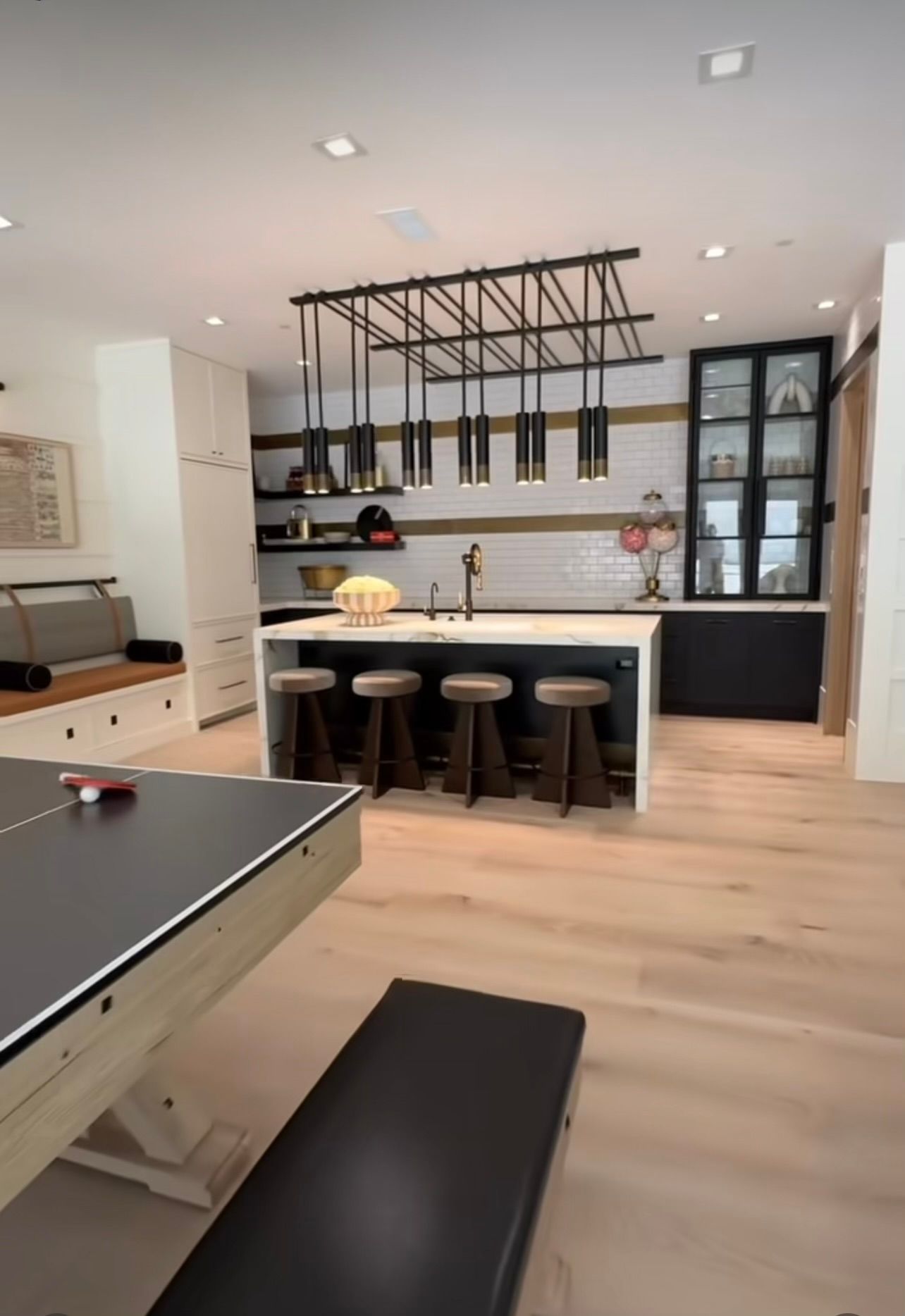 Modern kitchen and dining area with island seating, black accents, and pool table in foreground