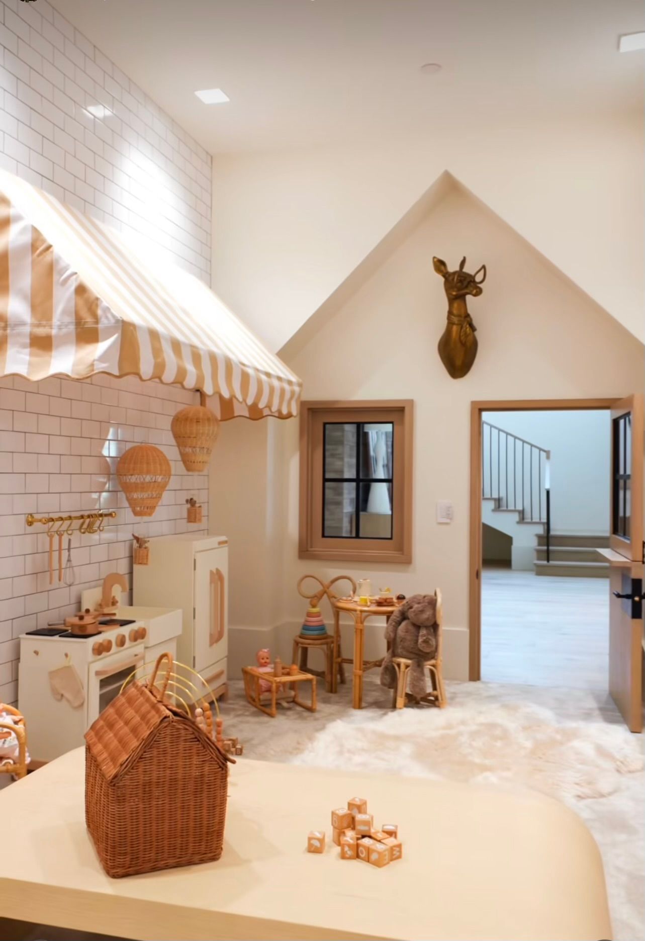 Miniature playroom with white walls, wicker toys, a striped canopy, and a deer head mounted above a doorway