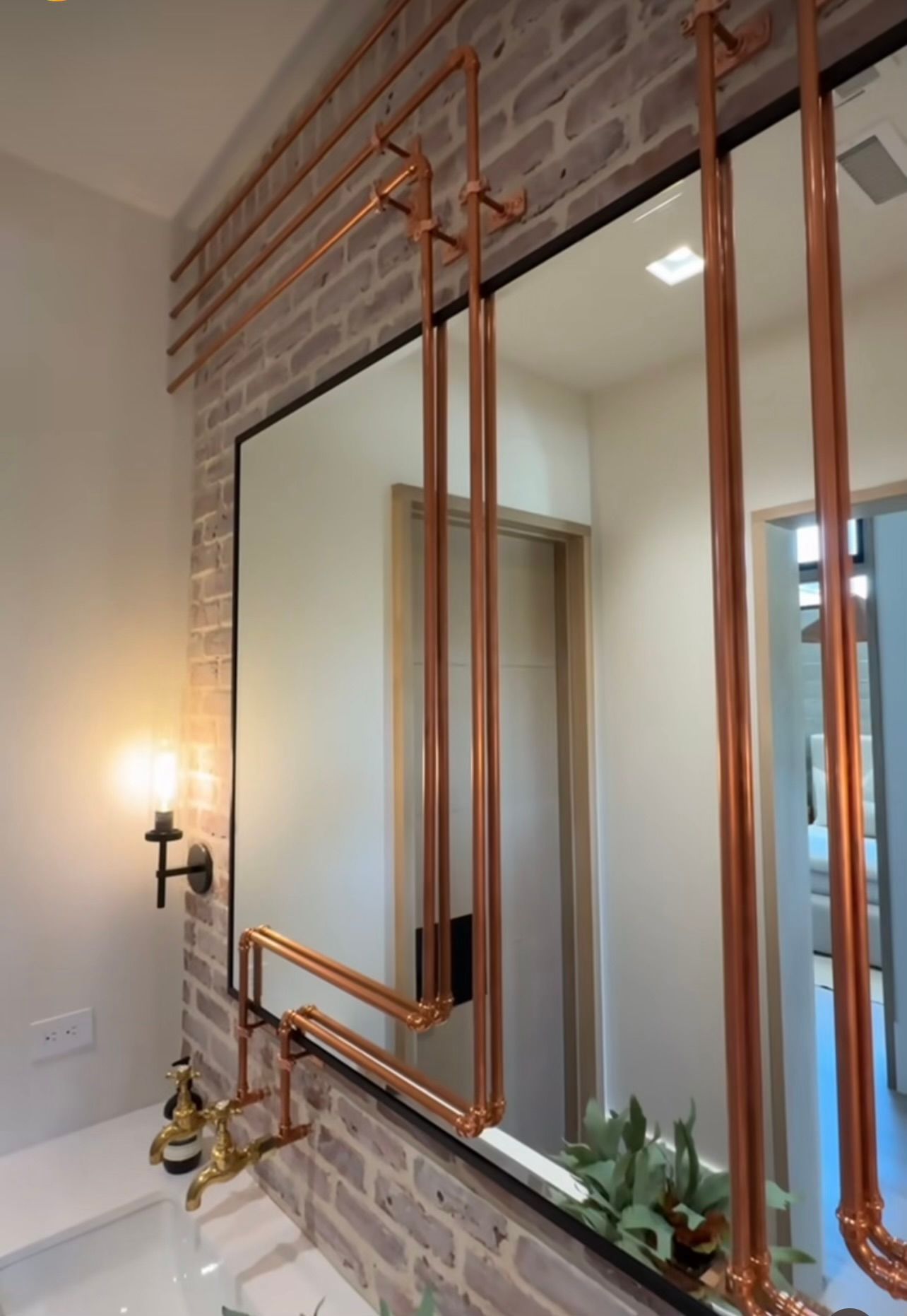 Copper-framed wall mirror above a white sink in a brick-accented bathroom or vanity area