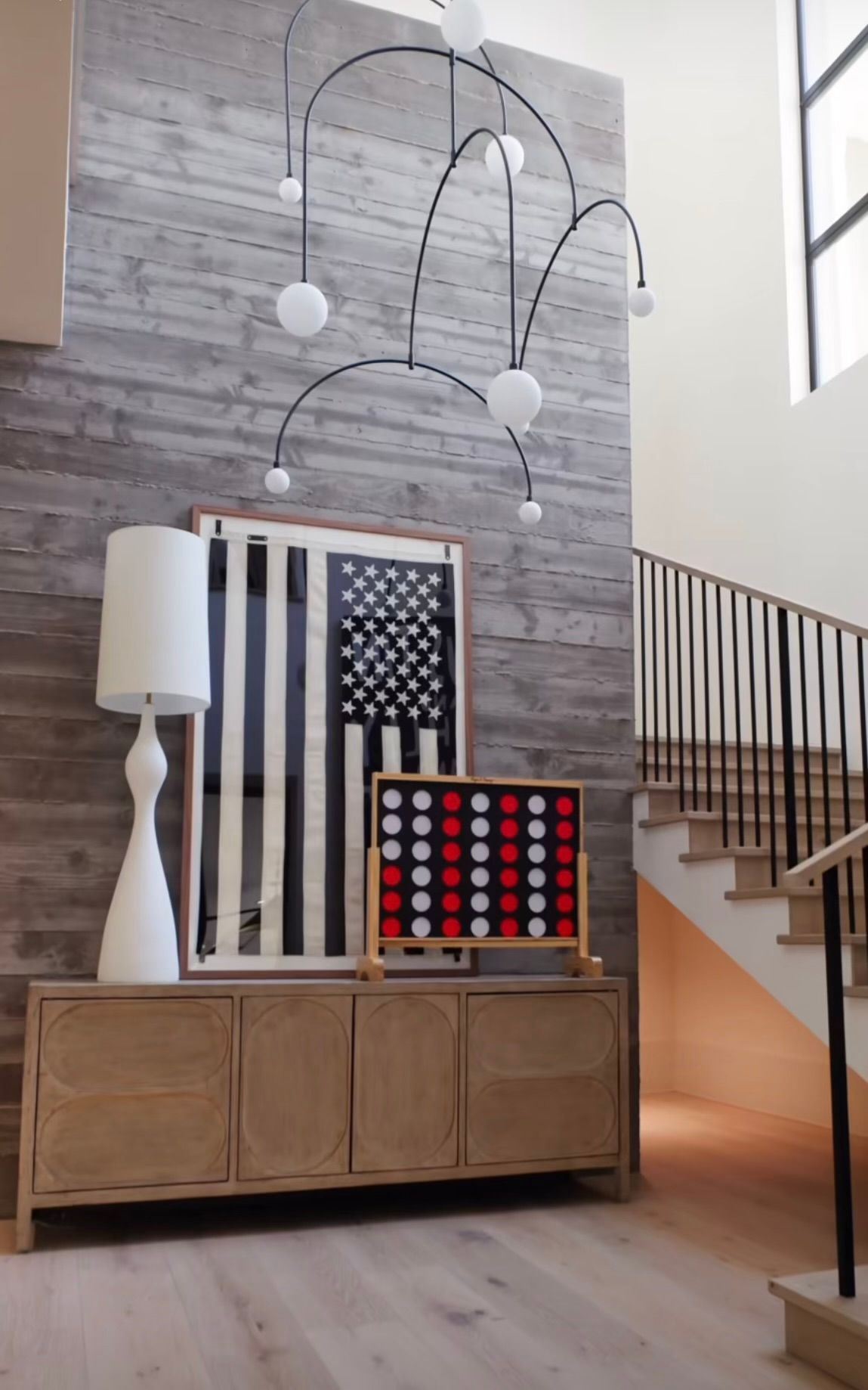 Modern foyer with wood credenza, colorful wall art, white floor lamp, staircase, and hanging globe sculpture