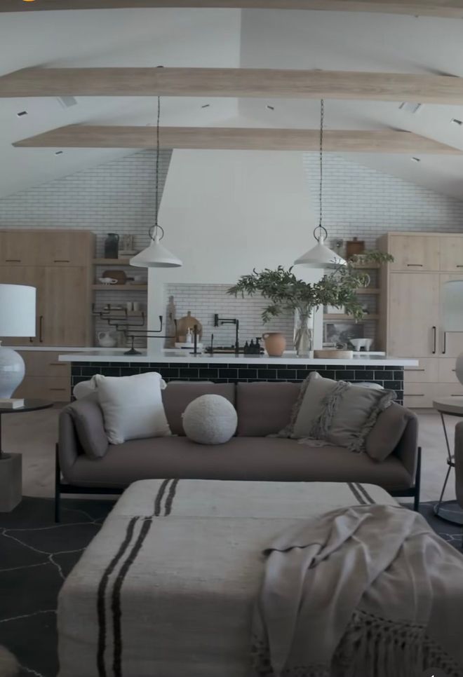 Modern living room with a gray sofa, pendant lights, wood accents, and large mirror over a kitchen counter