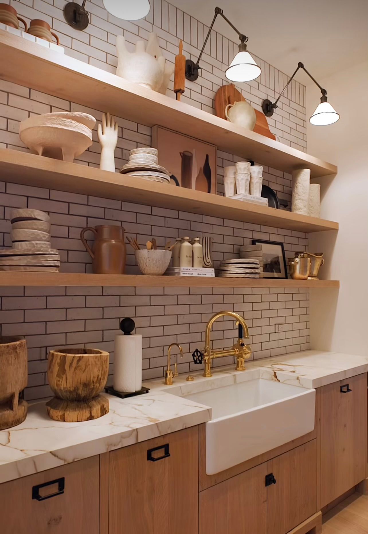 Modern kitchen with open wooden shelves, white subway tile, and farmhouse sink beneath three pendant lights