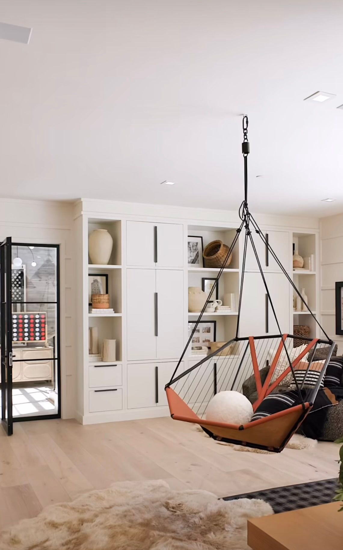 Bright living room with built-in cabinets and a hanging hammock chair on a wooden floor