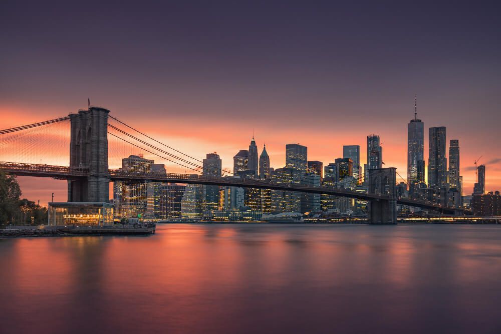 Un puente sobre un cuerpo de agua con el horizonte de una ciudad de fondo al atardecer.