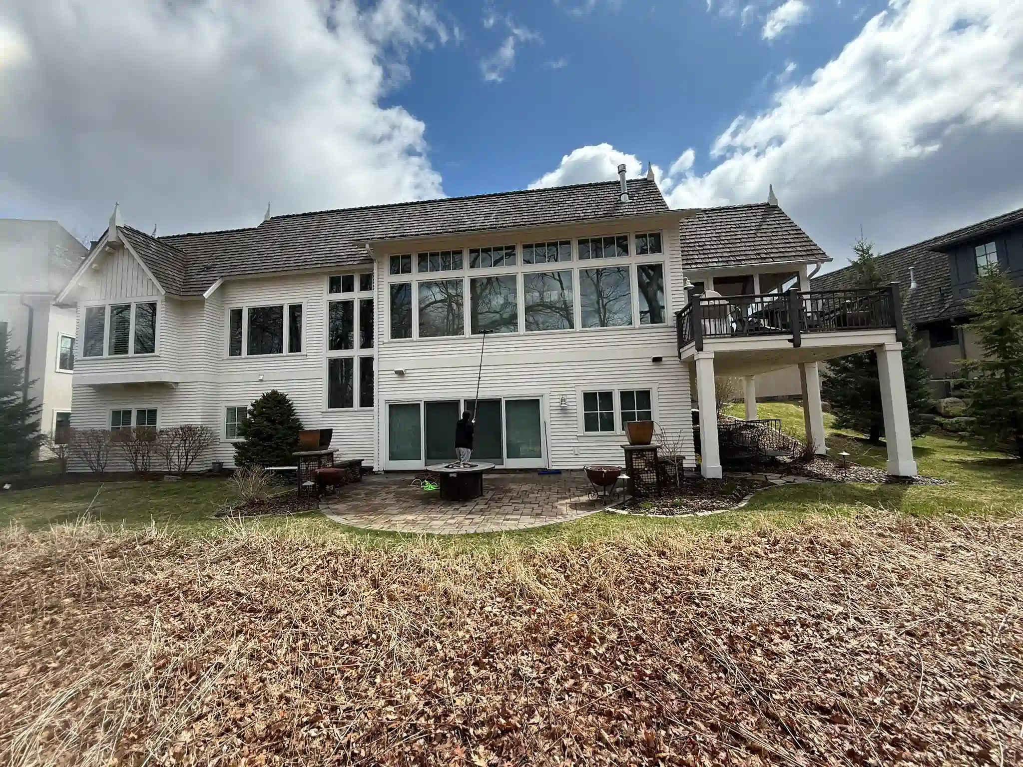 White house with many windows and a deck, seen from a grassy yard on a cloudy day.