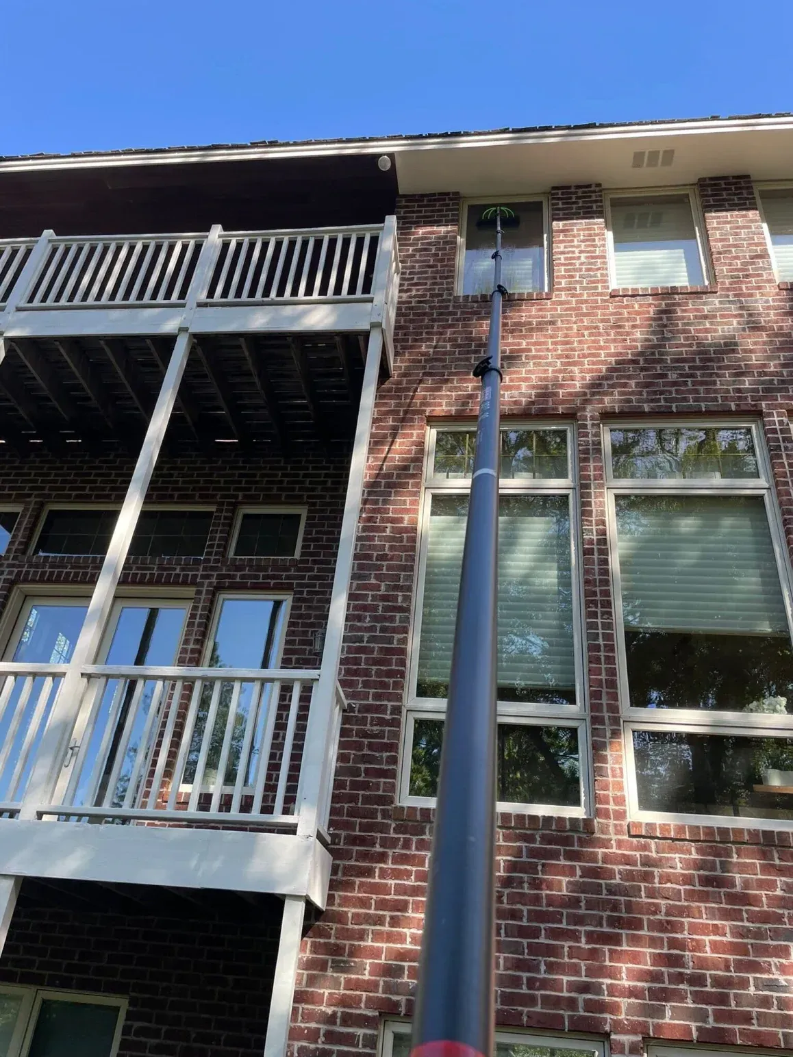 A window cleaner using a long pole to clean windows on a two-story brick building. Sunny day.
