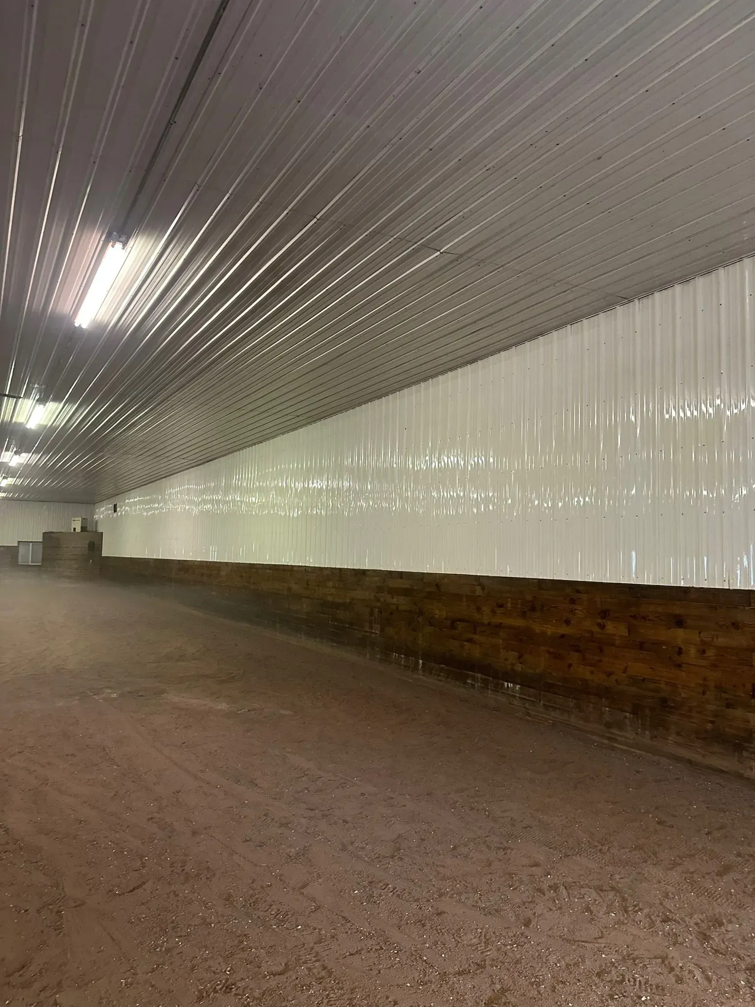 Indoor horse arena with dirt floor, white walls, and corrugated metal roof.