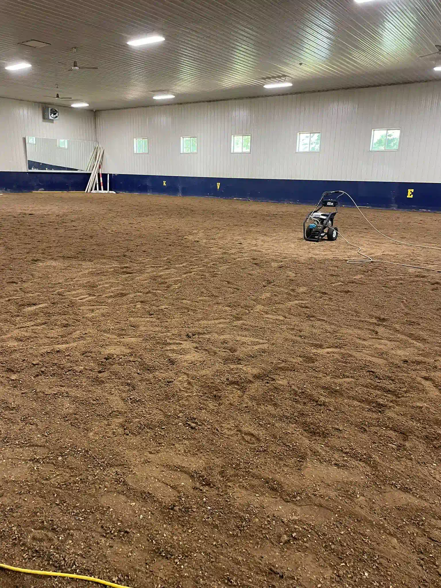 Indoor equestrian arena with a grooming machine. Arena is filled with brown footing.
