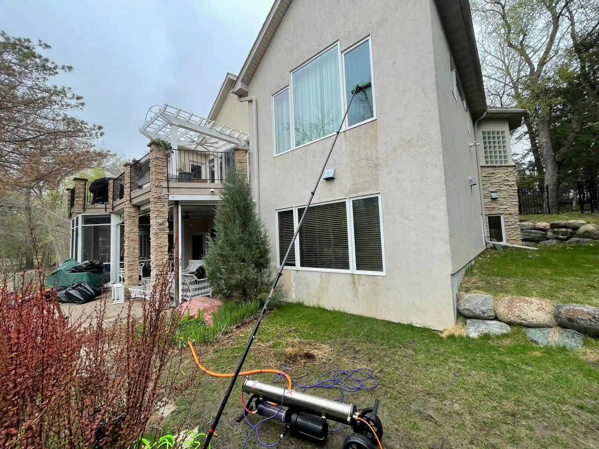 Cleaning windows on a stucco house using a water-fed pole system; outdoor setting, cloudy day.
