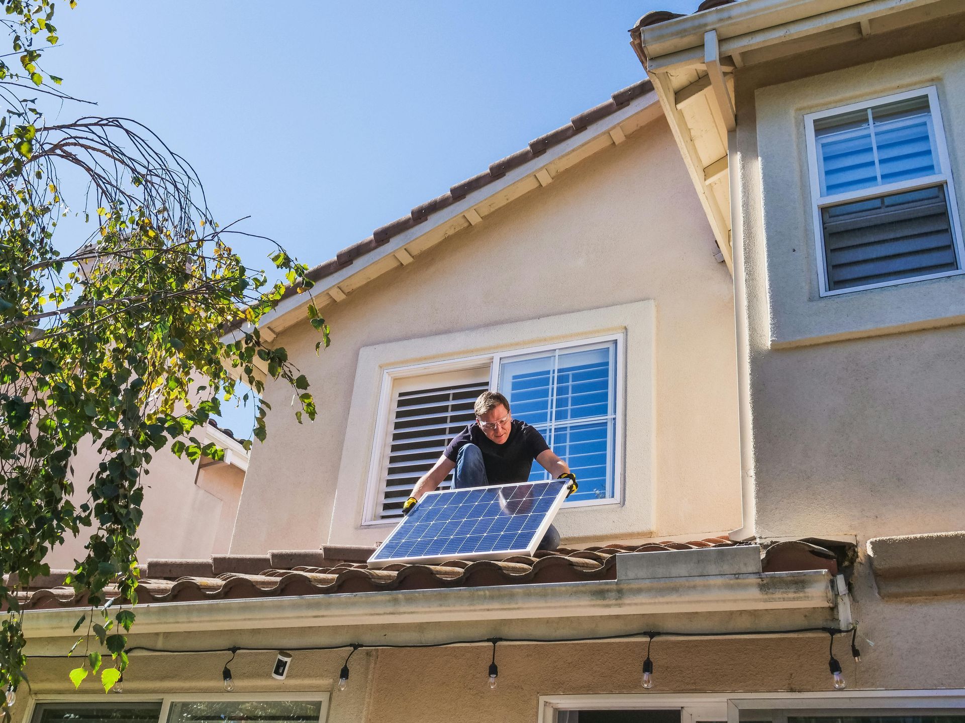 Man installing solar panel on a rooftop near a window on a sunny day.