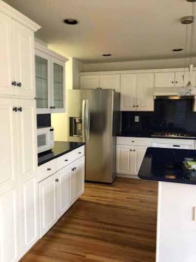 White kitchen with stainless steel appliances, dark countertops, and wood floors.