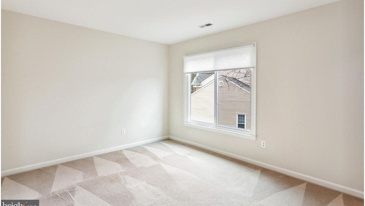 Empty room with beige carpet and walls, window with shade.
