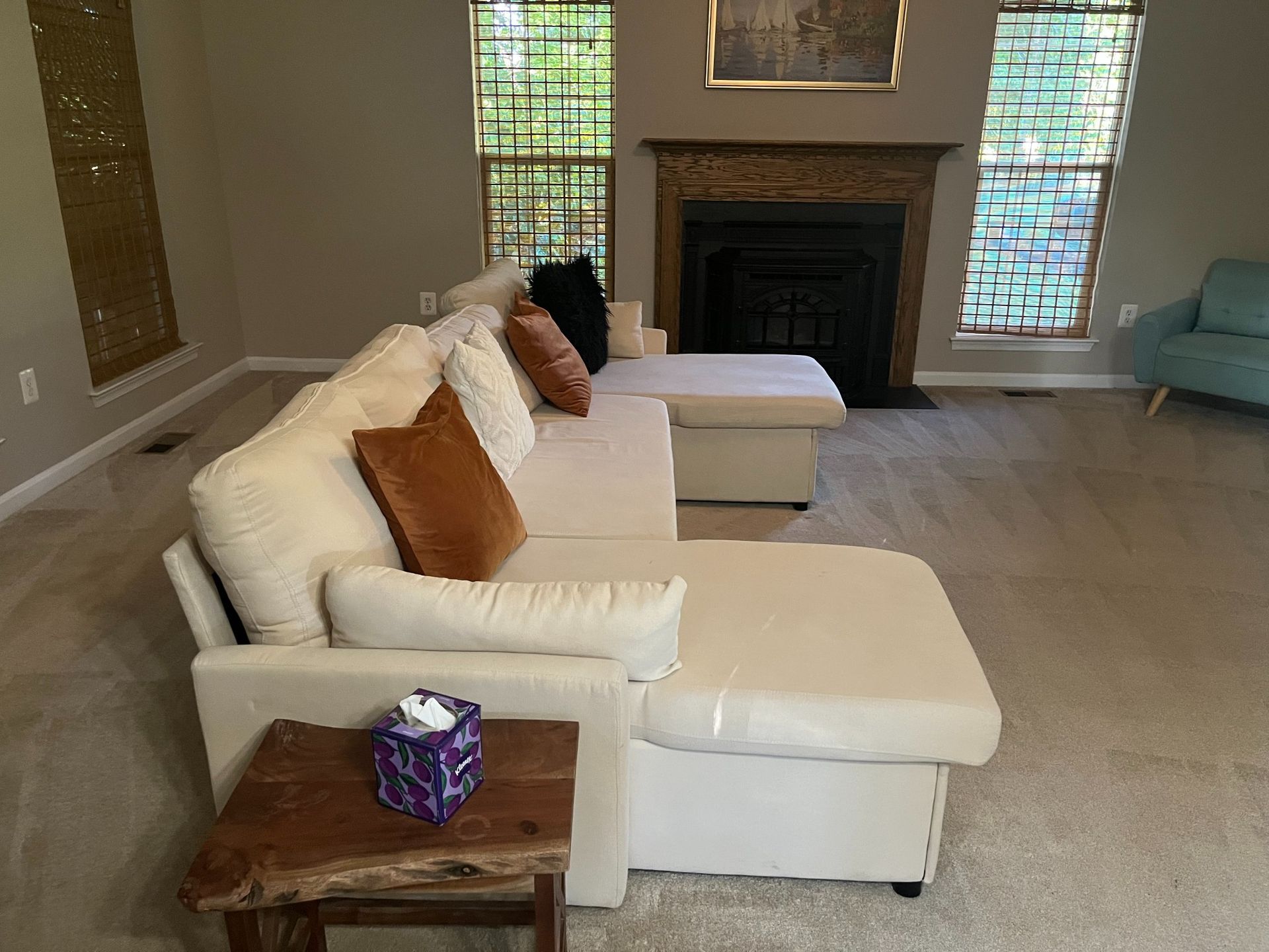 Living room with beige sectional sofa, fireplace, windows, and small wood side table.