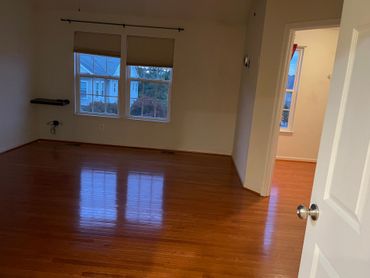 Empty room with wood flooring, windows, and an open doorway.