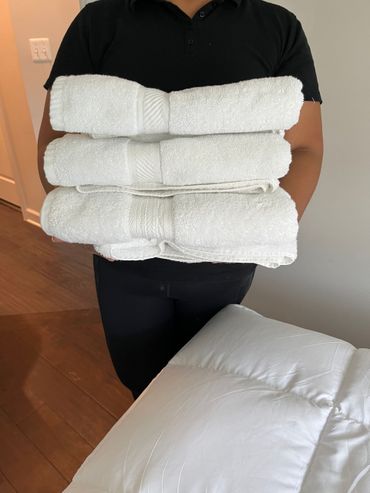 Person holding folded white towels, with a fluffy white blanket visible.