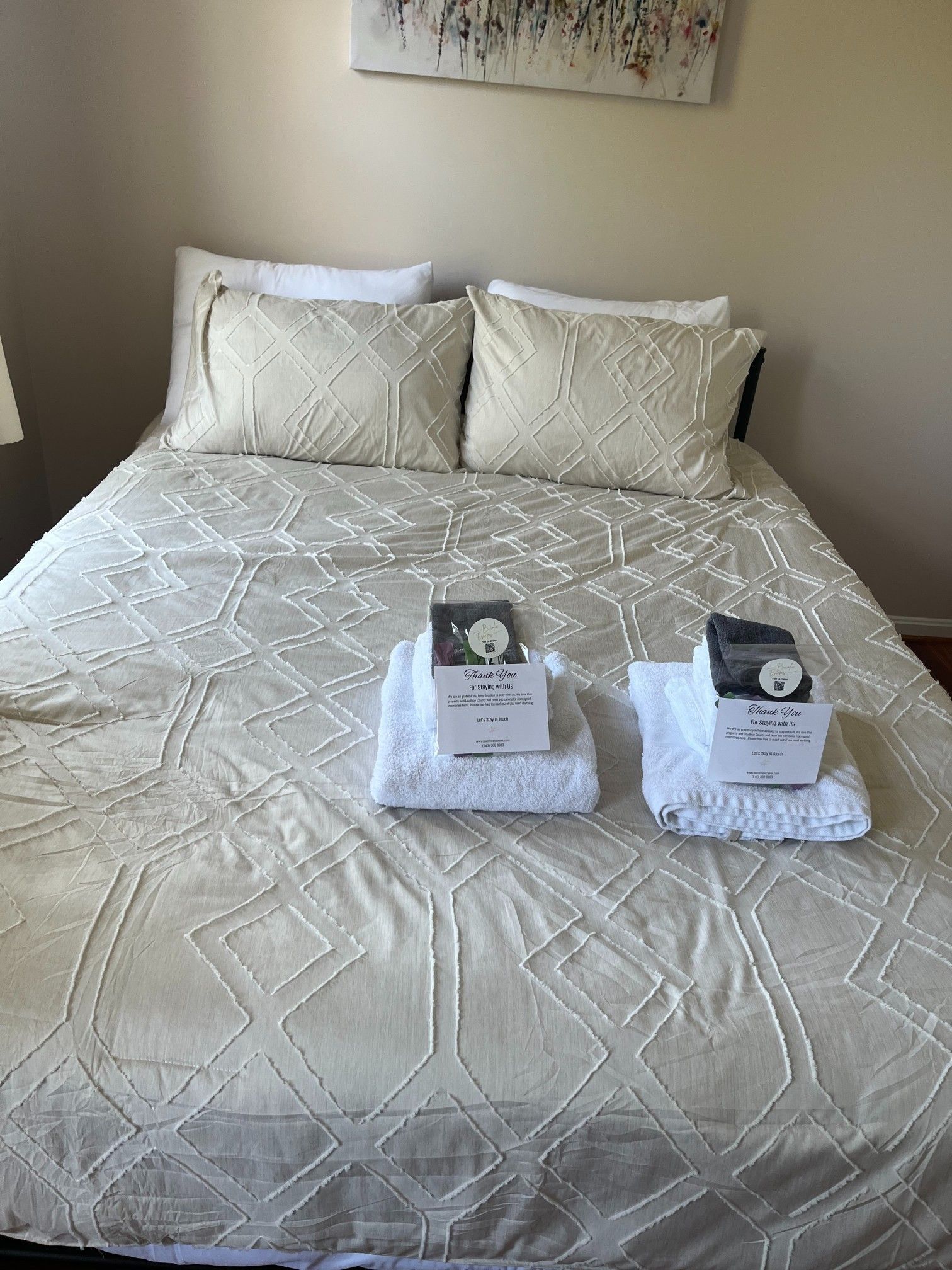 Bed with cream-colored geometric quilt and pillows. White towels with boxes are on top of the bed.