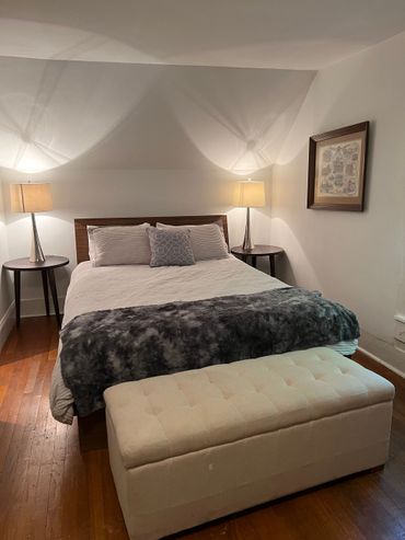 Bedroom with a bed, two nightstands, a bench, and a framed picture on the wall; brown hardwood floors.